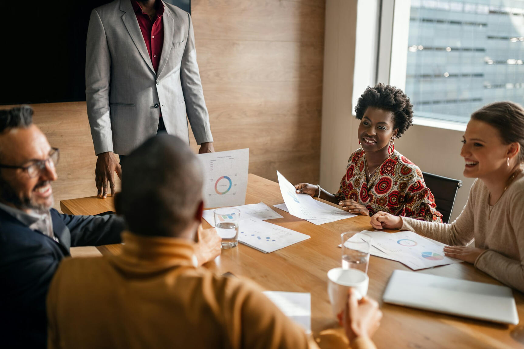A diverse group of professionals gathered around a meeting table smiling and reviewing documents
